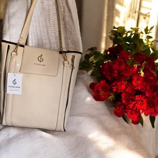 Beige handbag with visible brand logo next to a bouquet of red flowers on a light surface.